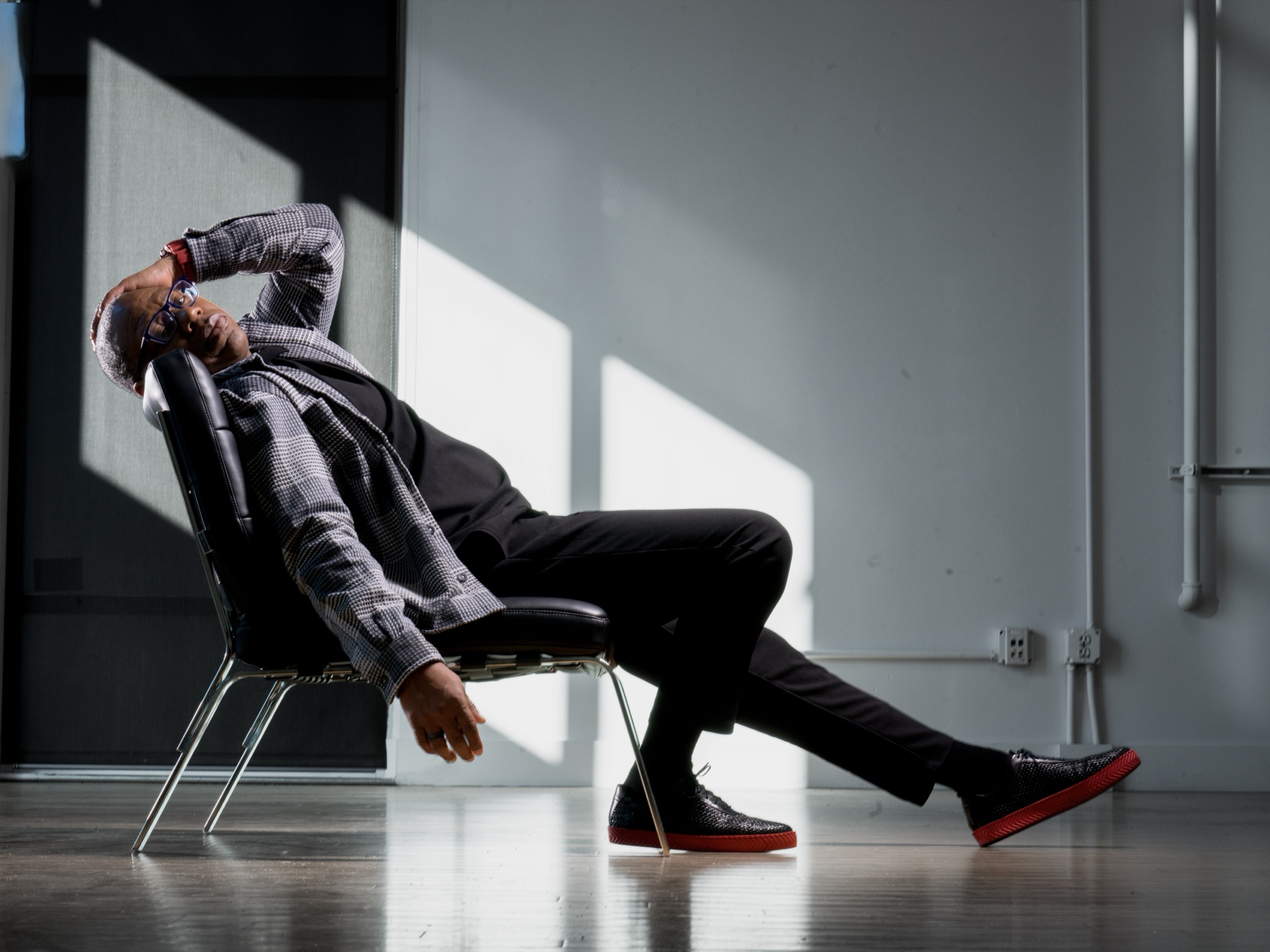 Will the Show reclining in a chair in the Uptown Loft, plaid suit, daylight.